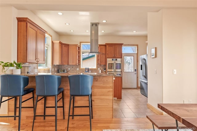 kitchen with a peninsula, appliances with stainless steel finishes, island range hood, and a breakfast bar area