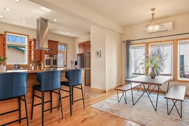 kitchen with island range hood, brown cabinetry, appliances with stainless steel finishes, and recessed lighting