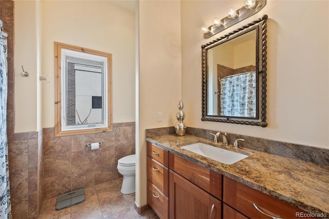 bathroom with vanity, tile patterned flooring, a wainscoted wall, toilet, and tile walls