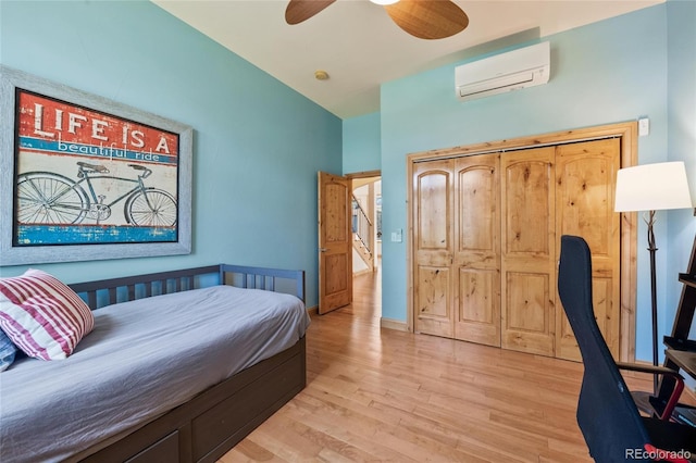 bedroom with light wood-style floors, a wall unit AC, and ceiling fan