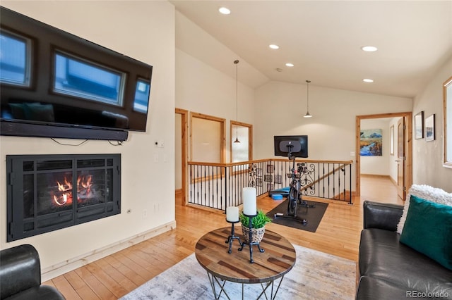 living area with a glass covered fireplace, baseboards, recessed lighting, lofted ceiling, and wood finished floors
