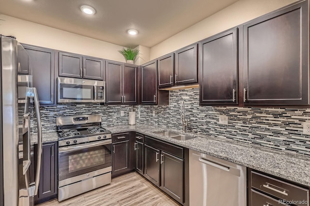 12856 Jasmine St Unit E, Thornton, CO 80602 - kitchen with appliances with stainless steel finishes, light stone countertops, decorative backsplash, dark brown cabinetry, and light wood-style floors