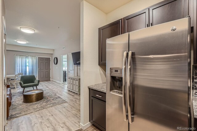 12856 Jasmine St Unit E, Thornton, CO 80602 - kitchen with stainless steel fridge, dark brown cabinetry, light wood finished floors, and light stone counters