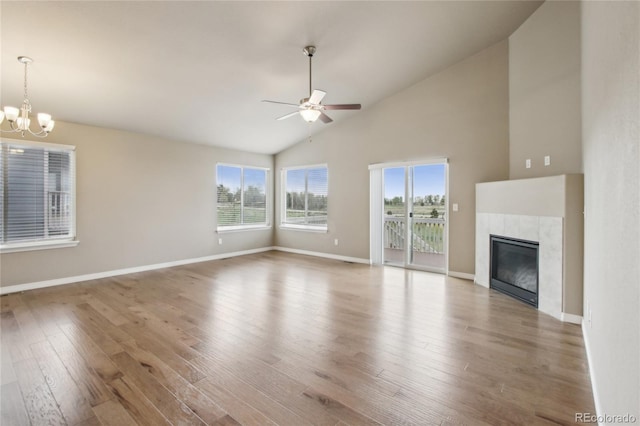 unfurnished living room featuring a fireplace, high vaulted ceiling, ceiling fan with notable chandelier, baseboards, and wood finished floors