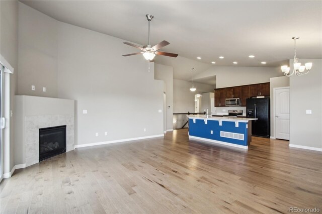 unfurnished living room with a tile fireplace, high vaulted ceiling, baseboards, ceiling fan with notable chandelier, and light wood-style flooring