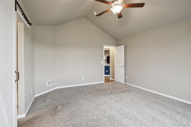 carpeted empty room featuring a barn door, a ceiling fan, baseboards, vaulted ceiling, and visible vents