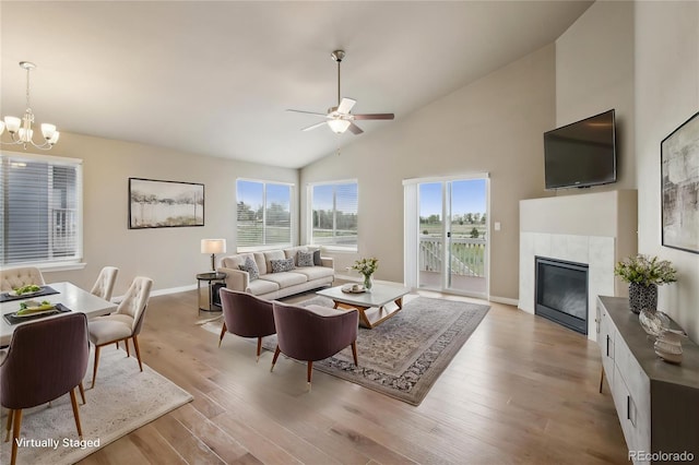 living room featuring a tiled fireplace, baseboards, high vaulted ceiling, ceiling fan with notable chandelier, and light wood-style flooring
