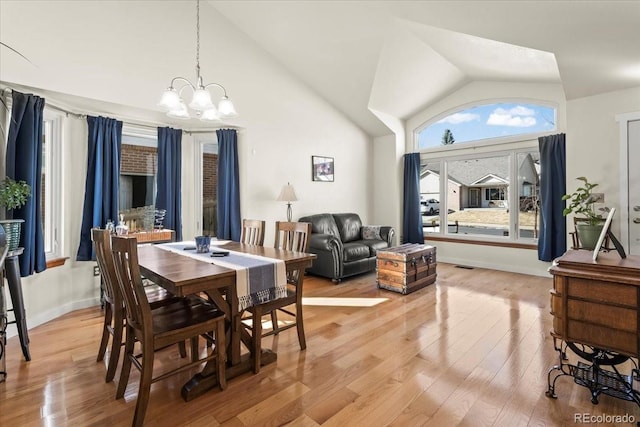 dining area featuring a chandelier, high vaulted ceiling, light wood-style flooring, visible vents, and baseboards