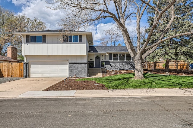 split level home with concrete driveway, an attached garage, fence, and a front yard
