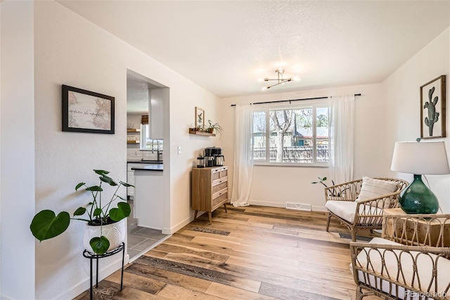 sitting room with baseboards, a chandelier, light wood-style flooring, and visible vents