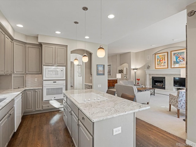 kitchen featuring white appliances, gray cabinets, a kitchen island, a tiled fireplace, and decorative light fixtures