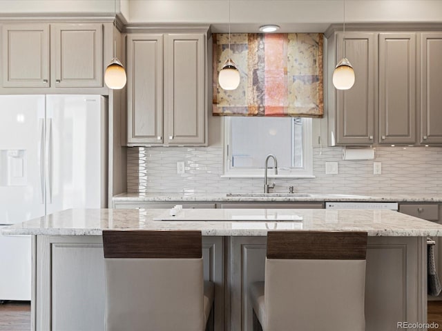 kitchen with light stone counters, sink, decorative light fixtures, and white fridge with ice dispenser