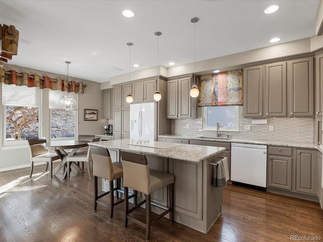 kitchen featuring sink, light stone counters, a center island, hanging light fixtures, and white appliances