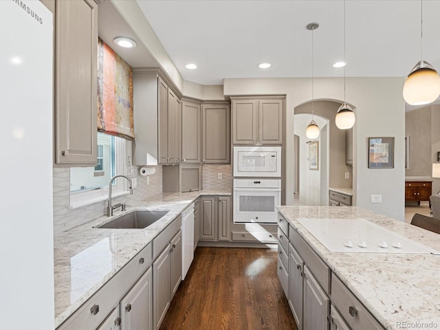 kitchen featuring pendant lighting, sink, white appliances, light stone countertops, and dark hardwood / wood-style flooring