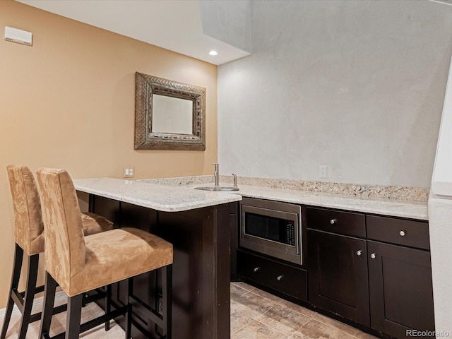 kitchen featuring sink, stainless steel microwave, light stone counters, a kitchen bar, and kitchen peninsula