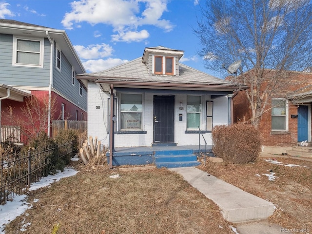 bungalow-style home with fence, a porch, and brick siding