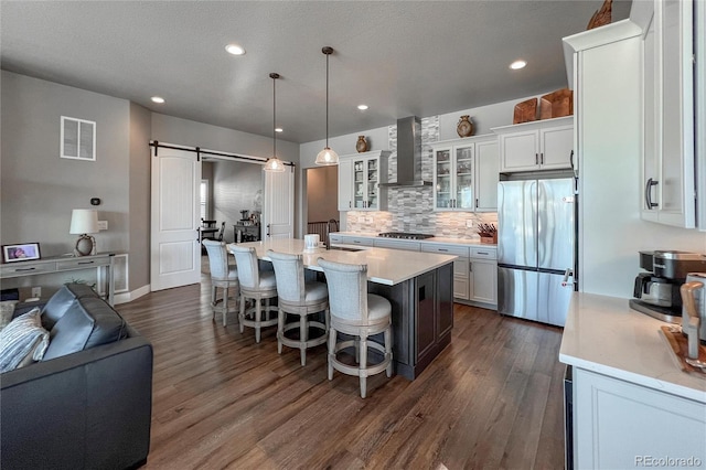 kitchen featuring pendant lighting, wall chimney range hood, a barn door, appliances with stainless steel finishes, and white cabinetry