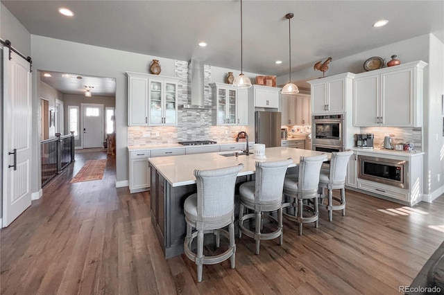 kitchen with sink, hanging light fixtures, wall chimney range hood, a barn door, and white cabinets