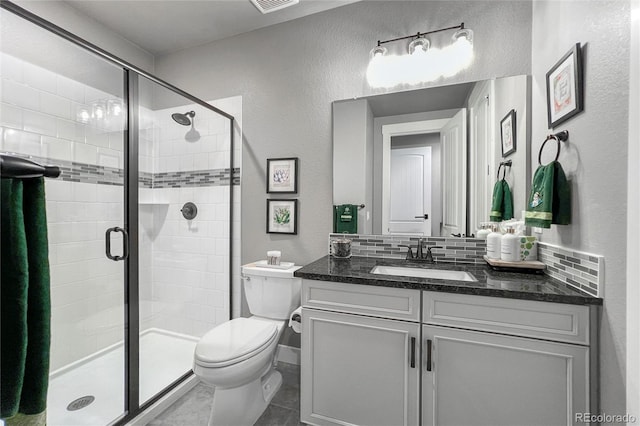 bathroom featuring tasteful backsplash, vanity, tile patterned flooring, toilet, and a shower with shower door