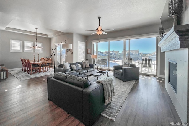 living room featuring a raised ceiling, ceiling fan, a water view, and dark wood-type flooring