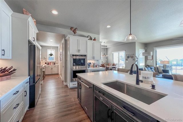 kitchen with white cabinetry, sink, stainless steel appliances, pendant lighting, and wood-type flooring