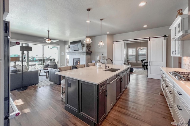 kitchen with ceiling fan, sink, a barn door, a center island with sink, and white cabinets