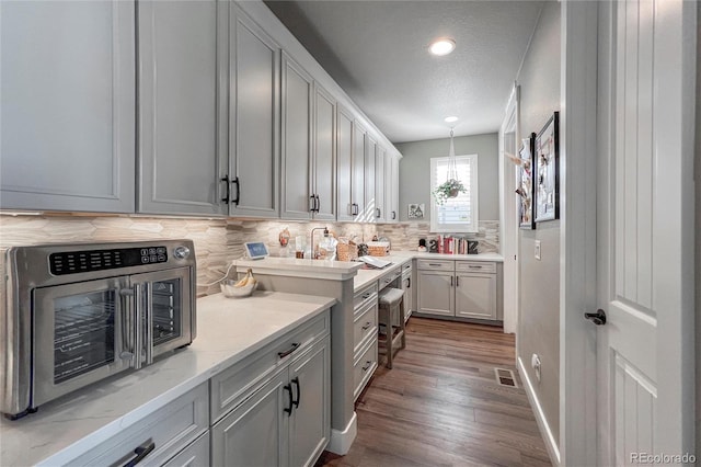 kitchen with gray cabinetry, hanging light fixtures, light stone countertops, a textured ceiling, and tasteful backsplash