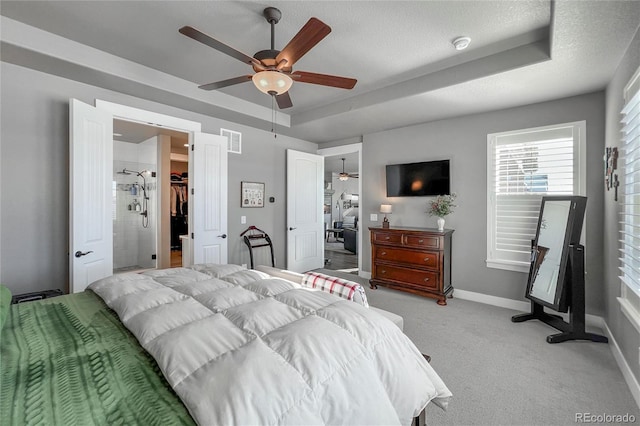 carpeted bedroom with ceiling fan, a raised ceiling, a textured ceiling, a walk in closet, and a closet