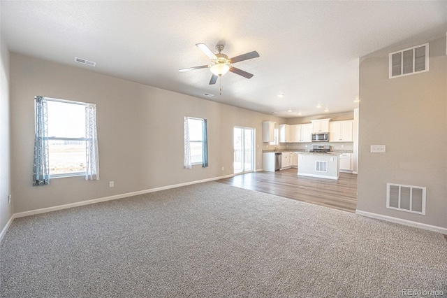 unfurnished living room featuring light colored carpet, a textured ceiling, and ceiling fan