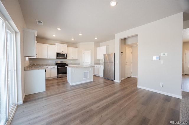 kitchen with white cabinetry, light stone counters, light hardwood / wood-style flooring, appliances with stainless steel finishes, and a kitchen island