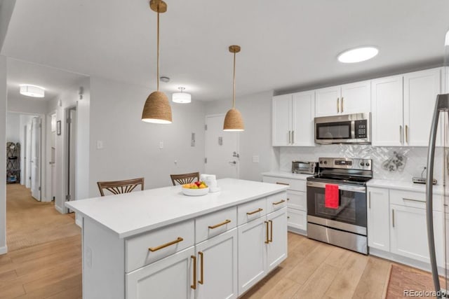 kitchen featuring tasteful backsplash, appliances with stainless steel finishes, white cabinets, and decorative light fixtures