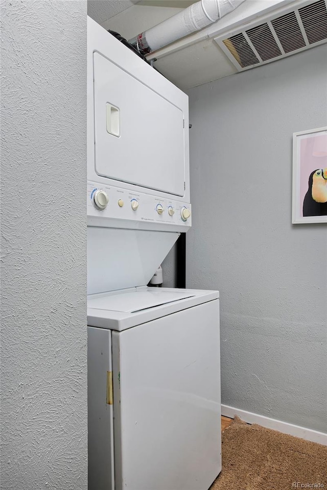 laundry room with stacked washer and dryer, baseboards, visible vents, a textured wall, and laundry area