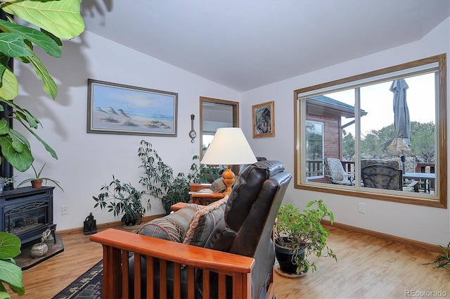 living room with vaulted ceiling, a wood stove, and light hardwood / wood-style floors