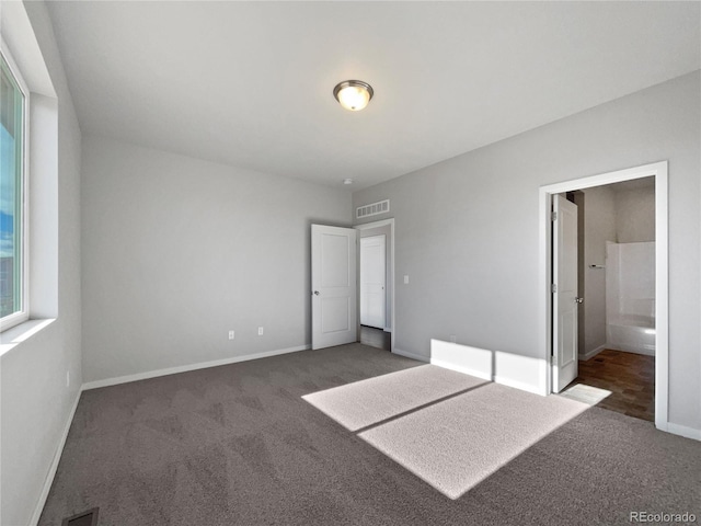 unfurnished bedroom featuring ensuite bathroom and dark carpet