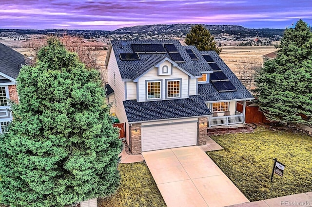 traditional home with a shingled roof, concrete driveway, covered porch, roof mounted solar panels, and brick siding