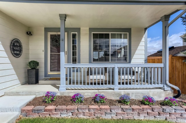 doorway to property with covered porch and fence