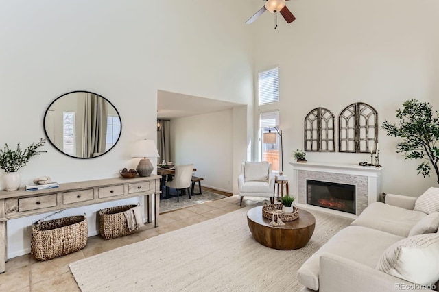 living room featuring ceiling fan, tile patterned flooring, a glass covered fireplace, and a towering ceiling