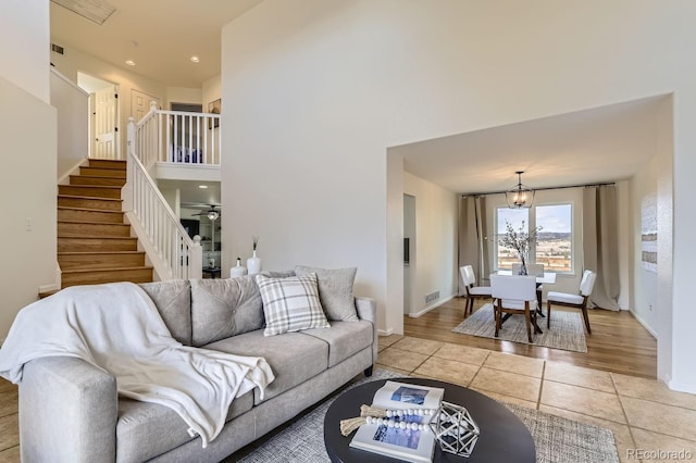 living area featuring light tile patterned floors, a towering ceiling, a chandelier, baseboards, and stairs