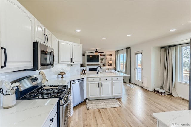 kitchen with a peninsula, stainless steel appliances, light wood-type flooring, white cabinetry, and a sink