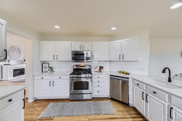 kitchen with light wood finished floors, appliances with stainless steel finishes, a sink, and white cabinets