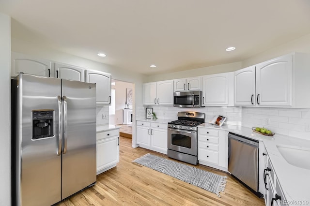 kitchen with light wood finished floors, recessed lighting, decorative backsplash, appliances with stainless steel finishes, and white cabinets