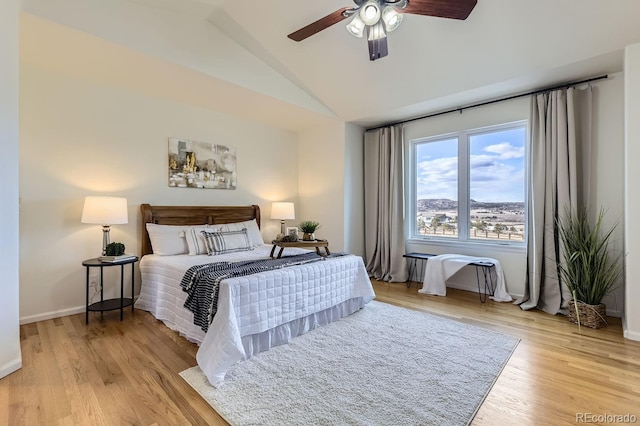 bedroom with light wood-type flooring, baseboards, vaulted ceiling, and a ceiling fan