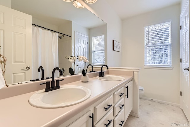 full bath featuring double vanity, a sink, toilet, and baseboards