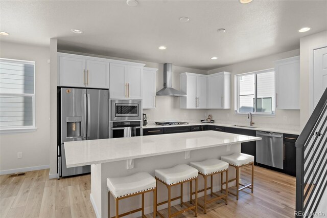 kitchen featuring wall chimney exhaust hood, sink, white cabinetry, appliances with stainless steel finishes, and a kitchen island