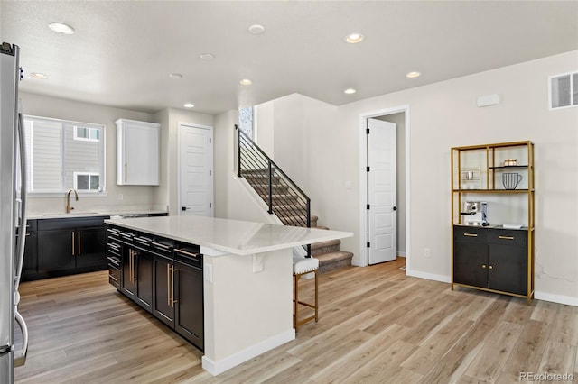 kitchen featuring sink, a breakfast bar area, light hardwood / wood-style floors, white cabinets, and a kitchen island