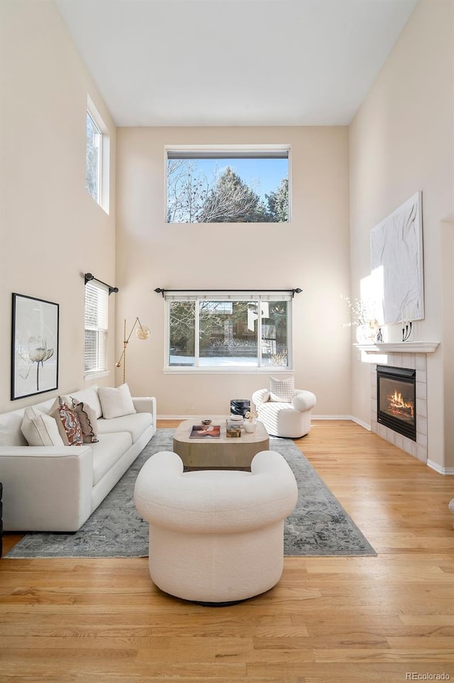 living room featuring a towering ceiling, a tiled fireplace, and light hardwood / wood-style flooring