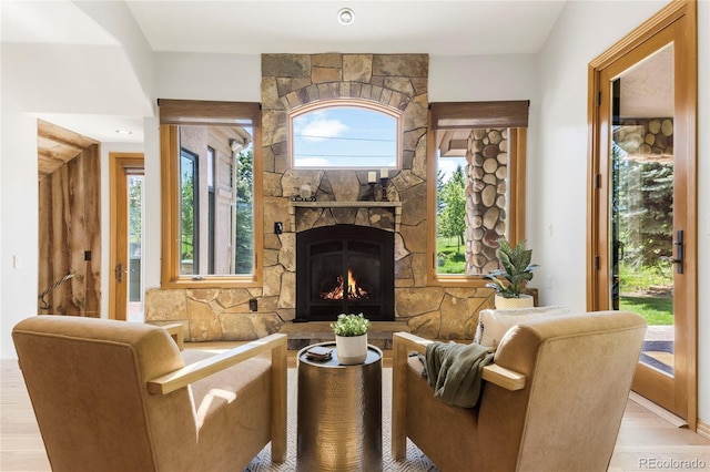 living area featuring a stone fireplace, light wood-style flooring, and healthy amount of natural light