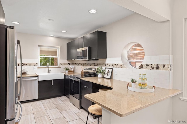 2880 N Glencoe St, Denver, CO 80207 - kitchen with stainless steel appliances, dark cabinets, a peninsula, decorative backsplash, and light stone counters