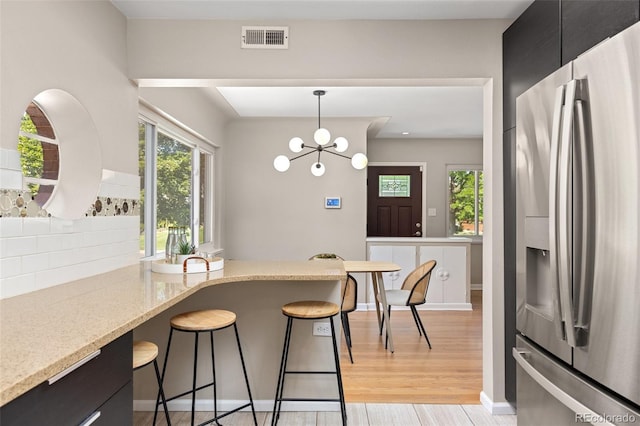 2880 N Glencoe St, Denver, CO 80207 - kitchen with stainless steel fridge with ice dispenser, dark cabinets, a breakfast bar area, backsplash, and light wood-style floors