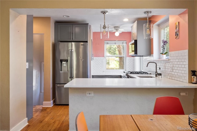 kitchen featuring appliances with stainless steel finishes, light hardwood / wood-style flooring, kitchen peninsula, and pendant lighting